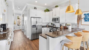 A modern kitchen with white cabinetry, stainless steel appliances, and a central island with bar stools. - 5 Bedroom Resort Villa w/Private Pool + Hot Tub | 1 Exit from Disney (Kissimmee)