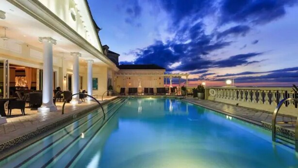A pool area with a view of the sunset, a covered seating area, and a building with columns. - 5 Bedroom Resort Villa w/Private Pool + Hot Tub | 1 Exit from Disney (Kissimmee)