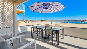 Ein Balkon mit Tisch, Stühlen und Sonnenschirm, mit Blick auf Strand und Boote.