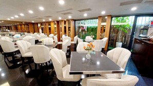 Un restaurante con sillas y mesas blancas, un reloj en la pared y vistas a zonas verdes.