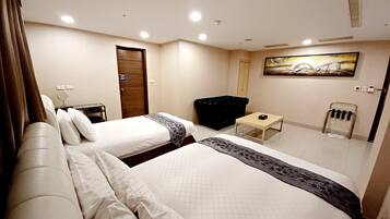 A hotel room with two beds, a small table, a chair, a painting on the wall, and a door.