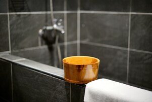 A bathroom with a wooden bowl on a counter, a white towel, and a shower with a chrome faucet.