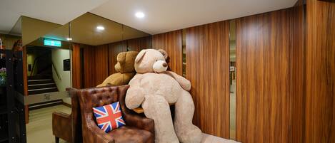 Un vestíbulo con una pared de madera, un sillón de cuero marrón y una almohada con la bandera Union Jack, y un gran oso de peluche apoyado contra la pared.