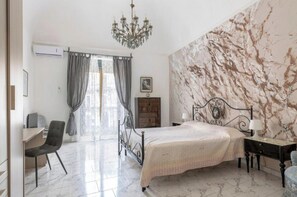 A bedroom with a bed, a desk, a chair, a chandelier, and a marble-patterned wall. - Grandma Lilla luxury home (Catania)