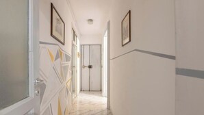 A hallway with a marble floor, white walls, and framed pictures on the walls.