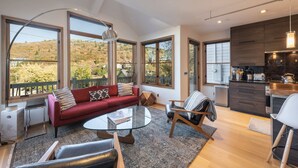 A spacious living area with a red sofa, a glass coffee table, and a view of a hilly landscape through large windows.