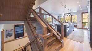 A modern kitchen with a central island, wooden staircase, and large windows.