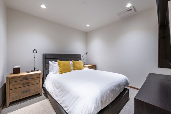 Um quarto moderno com uma cama, mesas de cabeceira, uma escrivaninha e uma televisão de tela plana.