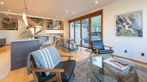 A modern living room with a glass coffee table, leather chairs, and a staircase leading to a balcony.