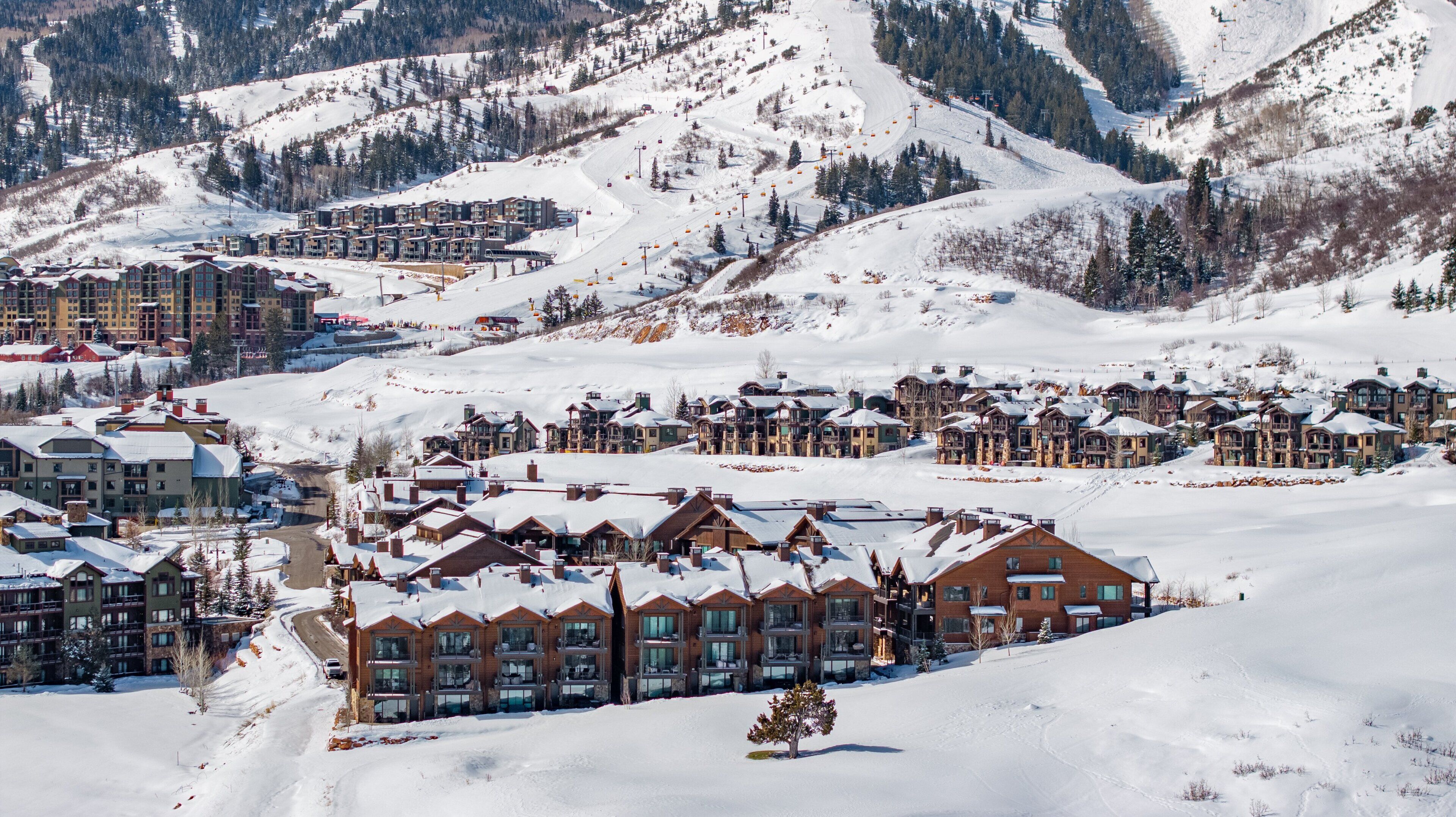A snow-covered resort with multiple buildings, ski lifts, and a mountainous backdrop.