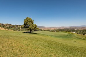 A golf course with a single tree, a flagstick, and a distant view of houses and hills. - Walk to Skiing Exceptional Juniper Landing 4 BR+Den Private Hot Tub Panoramic Golf Course Views Pool (park city)