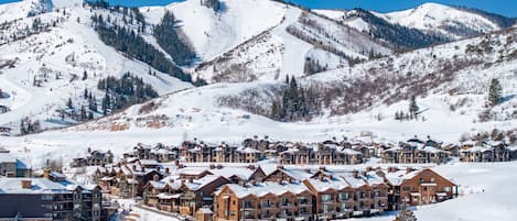 A snow-covered mountain resort with multi-story buildings, ski lifts, and a clear blue sky.