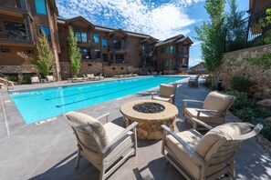 A pool area with lounge chairs and a fire pit, surrounded by stone walls and a multi-story building. - Walk to Skiing Exceptional Juniper Landing 4 BR+Den Private Hot Tub Panoramic Golf Course Views Pool (park city)