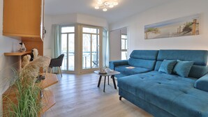 Een woonkamer met een blauwe bank, een kleine tafel, een stoel en uitzicht op de buitenwereld door een glazen deur.