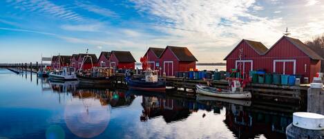 A waterfront scene with red buildings, boats, and calm water reflecting the structures.