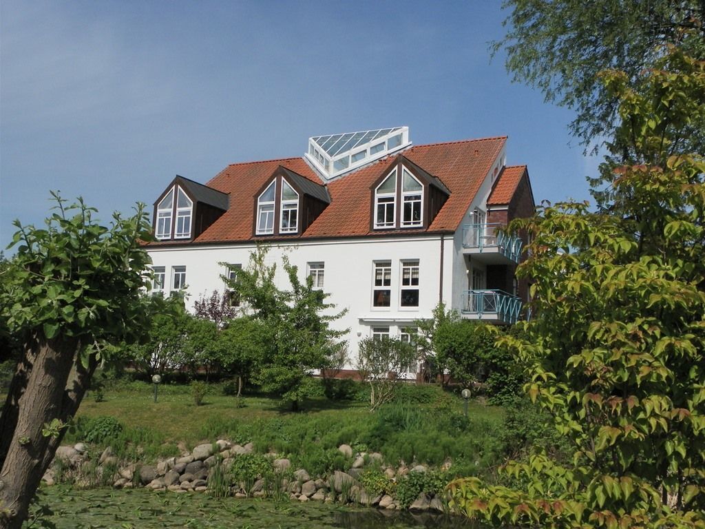Een huis met twee verdiepingen, voorzien van een rood dakbedekt met tegels, witte buitenmuren en een balkon op de bovenverdieping.