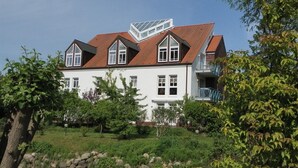 A two-story house with a red-tiled roof, white exterior walls, and a balcony on the upper floor. - Haus am Teich, Whg. D12 (Ostseebad Boltenhagen)