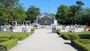 A gazebo with a stage, surrounded by benches and pathways in a park. - Haus am Teich, Whg. D12 (Ostseebad Boltenhagen)