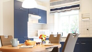 A modern kitchen with dark blue cabinets, a wooden dining table, and two chairs. - Haus am Teich, Whg. D12 (Ostseebad Boltenhagen)