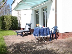 Eine Außenpatio mit Tisch, der mit einer blauen Tischdecke bedeckt ist, zwei Stühlen und einer Tischleuchte.