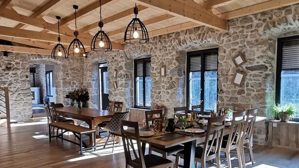 Un comedor amplio con una mesa y sillas de madera, paredes de piedra y lámparas colgantes.