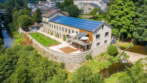 Un edificio grande con techo solar, rodeado de abundante vegetación y un río.