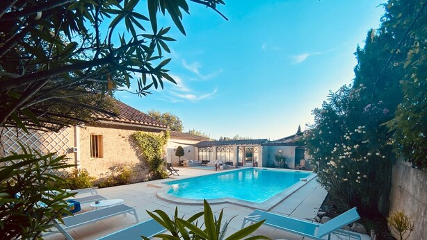 A swimming pool with lounge chairs and a small table, surrounded by a garden and a building with a tiled roof. - A l'Isle sur la Sorgue, charme provençal (L'Isle-sur-la-Sorgue)