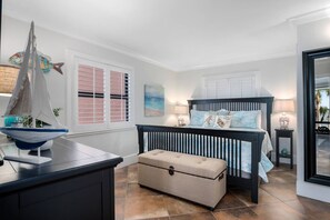 A bedroom with a bed, bedside tables, a chest of drawers, a window with shutters, and a decorative sailboat.