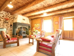 Una habitación acogedora con pared de piedra, vigas de madera en el techo, chimenea y dos sillas de madera con cojines rojos.