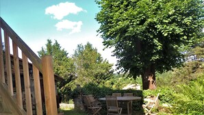 A wooden deck with a stone wall and a large tree providing shade. - Charming 19th-Century Farmhouse near Loire Gorges, Cozy Interior, Baby Equipment, Optional Services (Aurec-sur-Loire)