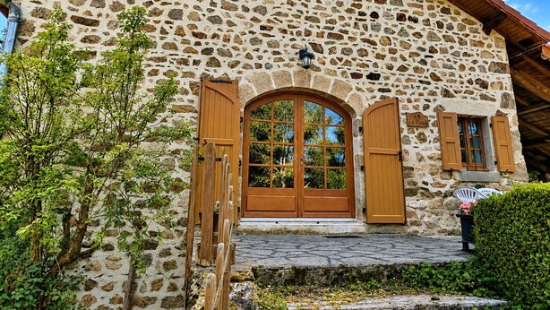 Ein Steinhaus mit einer Holztür und Fensterläden, einer Steintreppe und einem kleinen Fenster mit einem Schild.