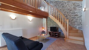En stue med en trætrappe, en stenvæg og en sort sofa.