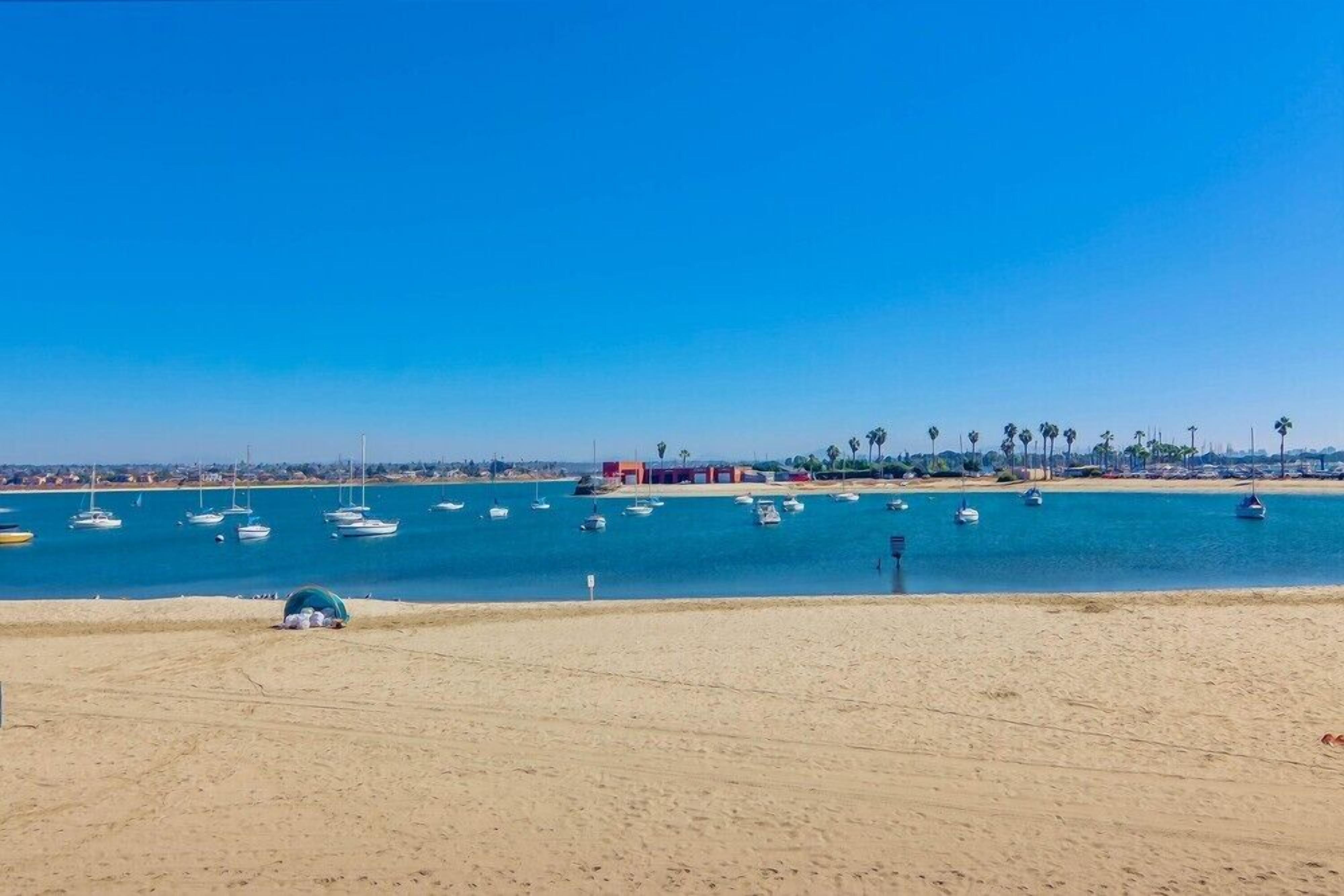 A beach with boats, a sandy shore, and a distant cityscape.