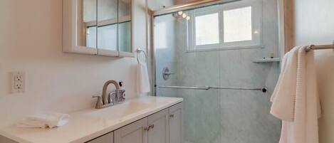 A modern bathroom with a glass-enclosed shower, a white vanity with a mirror, and a towel rack.