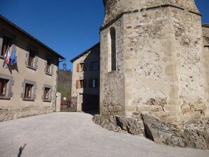 A stone building with a tower, a paved courtyard, and a flag. - Charming 10-Person Cottage in Idyllic Saint-Vert Setting (Saint-Vert)
