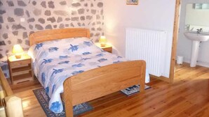 Une chambre avec un mur en pierre, un lit en bois, des lampes de chevet et un radiateur blanc.