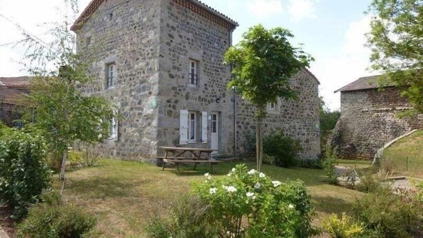 Un bâtiment en pierre avec un toit en tuiles, un petit porche et une table de pique-nique devant.