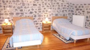 Une chambre avec deux lits simples, des tables de chevet en bois et un mur en pierre.