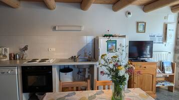 Une cuisine avec des poutres en bois, un réfrigérateur, une cuisinière et une table à manger recouverte d’une nappe à motifs floraux.