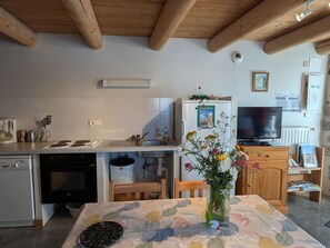 A kitchen with wooden beams, a refrigerator, a stove, and a dining table with a floral tablecloth.