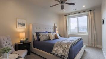 A bedroom with a bed, a nightstand, a chair, a table, a ceiling fan, and a window.