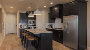 A modern kitchen with dark cabinetry, stainless steel appliances, and a central island with bar stools.