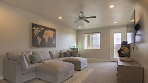 A living room with a sectional sofa, a ceiling fan, a world map artwork, and a large window.