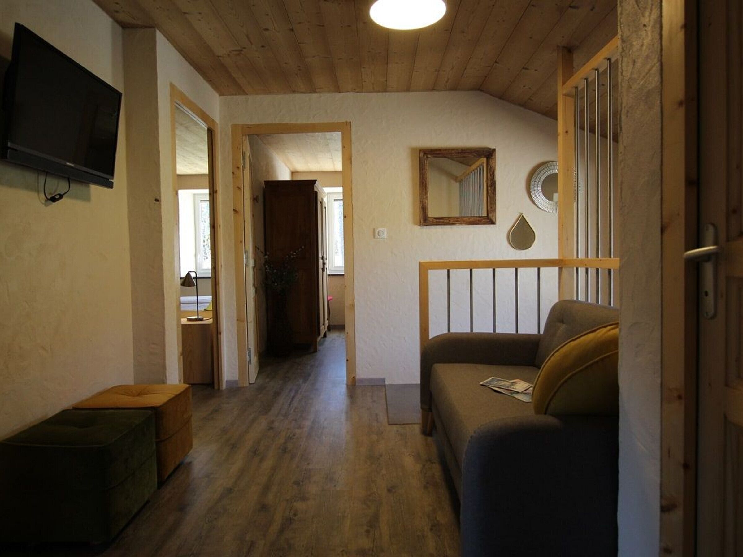 Una habitación acogedora con techo de madera, un televisor montado en la pared, un sofá y una mesita de noche con lámpara.