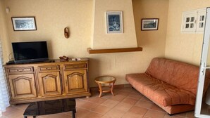 A living room with a wooden cabinet, a television, a sofa, a small round table, and a bench. - Maison Place manemeur (Quiberon)