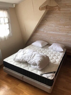 Ein Schlafzimmer mit einem Bett, einem Fenster mit Vorhängen, einer Holzwand und einem Deckenventilator.