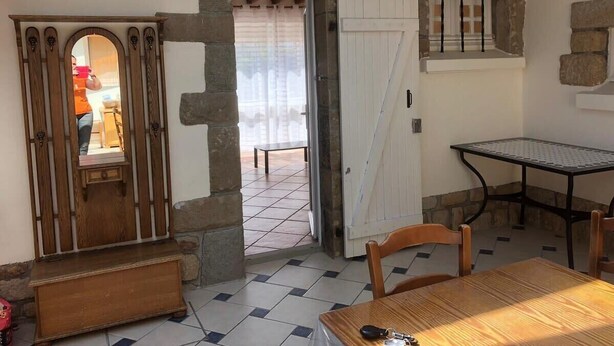 A room with a wooden bench, a table, and a door leading to an outdoor area with a bench. - Maison Place manemeur (Quiberon)