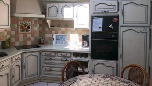 A compact kitchen with white cabinetry, a tiled backsplash, a refrigerator, and a stove. - Maison Place manemeur (Quiberon)