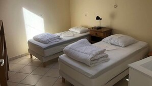 A hotel room with two beds, a bedside table with a lamp, and a window providing natural light. - Maison Place manemeur (Quiberon)