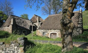 Un edificio de piedra con techo de paja, rodeado de follaje y árboles.